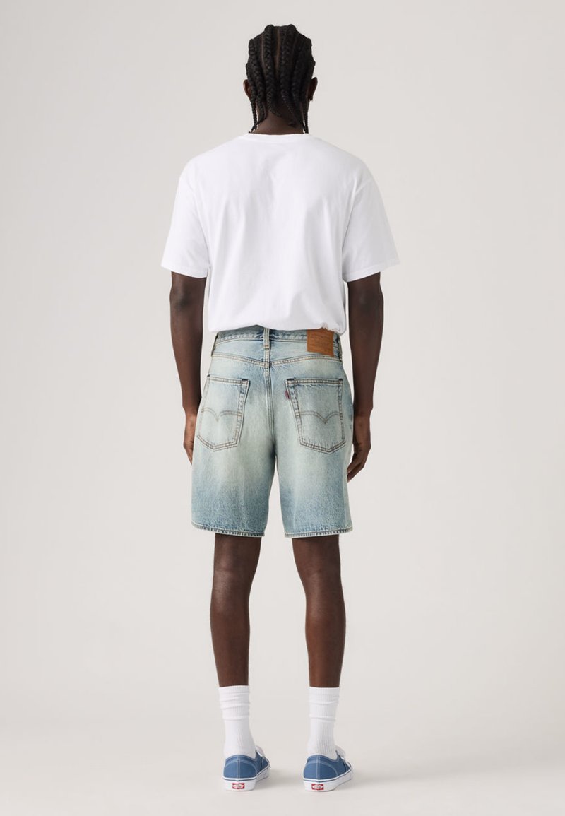 Shorts di jeans in lavaggio azzurro chiaro con taglio rilassato, dotati di due tasche posteriori e di un'etichetta in pelle marrone sulla cintura. Indossati con una maglietta bianca.
