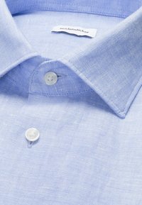 Chemise en lin bleu clair avec des boutons blancs et une étiquette de marque "seidensticker" visible à l'intérieur du col.