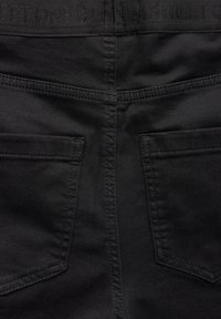 Zwart denim stof met een stevige textuur, twee achterzakken en stiksels. De tailleband heeft "DENIM STREET" geborduurd.