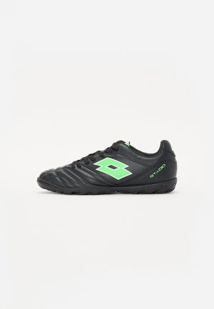 Black synthetic soccer shoes with textured surface, green logo, and accents. Features rounded toe, lace-up front, and rubber outsole.