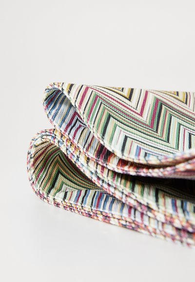 Multicolored table runner featuring a zigzag pattern with varied stripes in green, pink, yellow, and blue; textured fabric with folded edges.