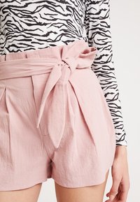 Shorts texturés roses avec un nœud à l'avant et un design plissé, portés sur un haut à manches longues arborant un motif zèbre noir et blanc.