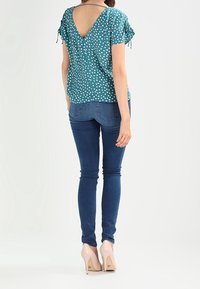 Blusa verde azulada con lunares blancos; diseño de espalda en V; mangas cortas con lazos. Se lleva con jeans ajustados de color azul oscuro y tacones de color beige claro.