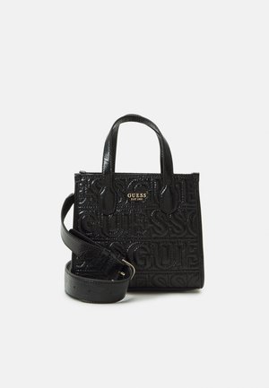 Sac à main noir avec logo "GUESS" en relief, en cuir texturé, double poignées et une sangle réglable. Forme rectangulaire compacte.