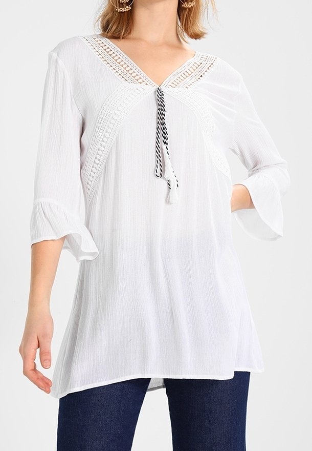 Top bianco fluido con scollatura a V e dettagli in crochet. Presenta un laccio con accenti in bianco e nero. Maniche a tre quarti.