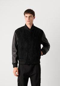 Black bomber jacket with suede body and leather sleeves. Features ribbed cuffs and hem, front buttons, and subtle brand logo.