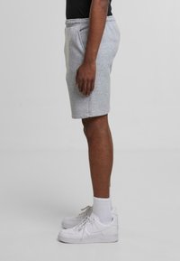 Grå, knælange sweatshorts med elastisk talje. Båret med hvide sneakers og ankelsokker. Sideværts, glat tekstur.