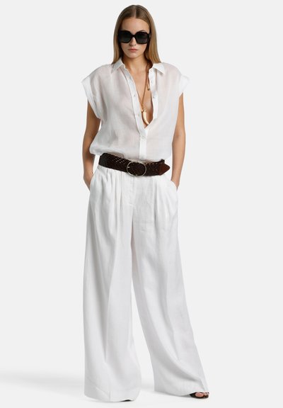 Camisa blanca de lino de botón con mangas cortas y escote profundo, combinada con pantalones blancos fluidos y un cinturón trenzado marrón. Gafas de sol negras.