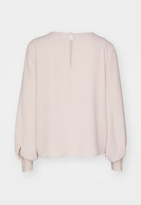 Light pink long-sleeve top with a round neckline, back keyhole opening, and buttoned cuffs. Textured fabric with a loose fit.