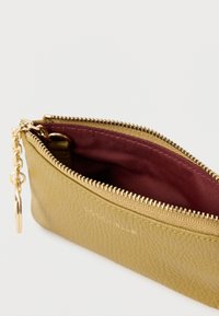 Aranyszínű, texturált bőr erszény bíborvörös béléssel, arany cipzárral és fém kulcstartóval. Szélessége fent szélesebb, alul keskenyedik.