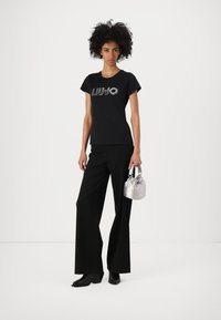 Black t-shirt with silver "LIU JO" lettering, paired with black wide-leg trousers and a small silver bag. Footwear features a chunky heel.