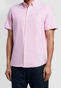 Camicia button-up rosa a maniche corte in tessuto di cotone; presenta una sottile trama, colletto e un piccolo logo ricamato sopra il lato sinistro del petto.
