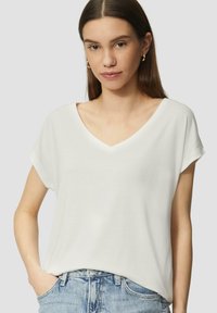 Biała koszulka typu V-neck z krótkim rękawem, wykonana z miękkiego materiału, charakteryzująca się luźnym krojem, zestawiona z jasnoniebieskimi dżinsami.