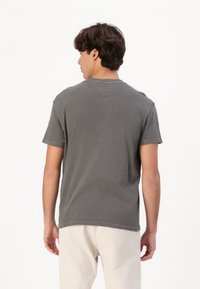 Camiseta de algodón gris con mangas cortas y escote redondo, con un logo sutil en la parte posterior. Textura suave y corte relajado.