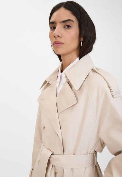 Trench coat beige con design doppiopetto, ampio colletto a punte e vita con cintura. Tessuto morbido, silhouette classica, vestibilità sartoriale.