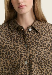 Een leopard print shirtjack in bruin en zwart, met drukknoopsluitingen, een kraag en twee borstzakken van een gestructureerde stof.