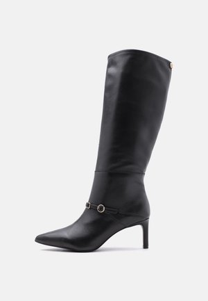 Botte en cuir noire montant jusqu'au genou, avec un bout pointu, un talon fin de hauteur moyenne, et une fine lanière décorative avec deux petites boucles.