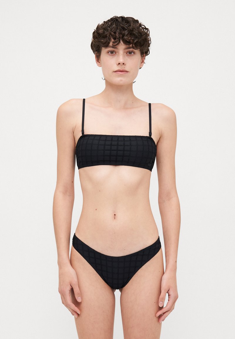 Crni bikini set s teksturiranim, rešetkastim uzorkom. Gornji dio ima tanke naramenice i bandeau dizajn; donji dio ima nisku struk i odgovarajući uzorak.