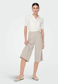Jasno beżowe kuloty z plisami, zestawione z białym, krótkim polo z prążkowanej tkaniny, z kołnierzykiem i guzikami. Gładka tekstura, casualowy design.