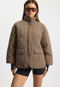 Quilted brown jacket with a high collar, two front pockets, and a zip closure; features a textured finish and a relaxed fit.
