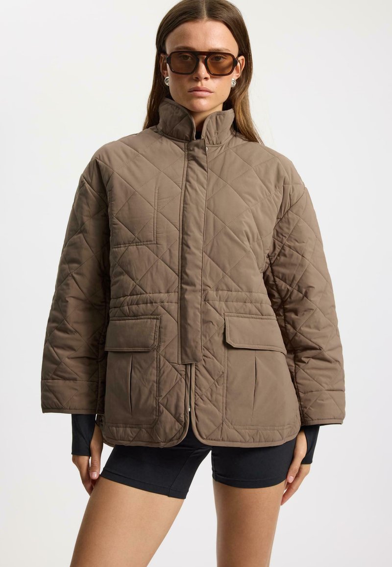 Quilted brown jacket with a high collar, two front pockets, and a zip closure; features a textured finish and a relaxed fit.