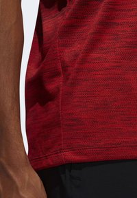 Camisa atlética roja con textura que presenta un patrón jaspeado, mangas cortas y un corte ajustado, combinada con pantalones negros.