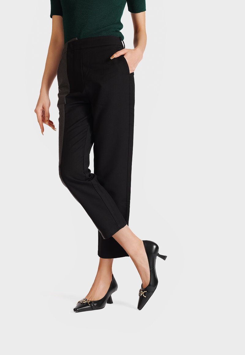 Pantaloni neri su misura con tasche laterali, abbinati a tacchi in pelle verniciata nera con dettagli accentuati nella parte anteriore e un'altezza del tacco contenuta.