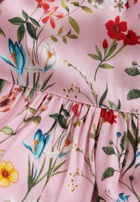 Rosa Stoff mit mehrfarbigem Blumenmuster, das blaue, rote und gelbe Blumen sowie grüne Blätter umfasst, mit versammeltem Nähdetail.