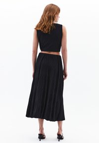 Zwart tweedelig outfit met een mouwloze cropped top en een lange, vloeiende rok met een textuurdesign. G gedragen met open teen hakken.