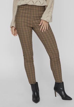 Pantalon skinny à carreaux bruns avec une taille haute, présentant une texture lisse et une finition sans plis, associé à des bottines noires.