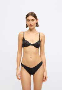 Ensemble de lingerie en dentelle noire comprenant un soutien-gorge triangle à fines bretelles et une culotte taille basse assortie, tous deux avec des bords ondulés et des motifs floraux.