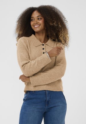 Pulover tricotat bej cu guler, patru nasturi negri și manșete cu nervuri. Purtați cu blugi din denim albastru. Textură moale.