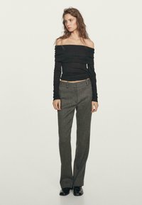 Schwarzes schulterfreies Langarmoberteil, kombiniert mit grauen hochgeschnittenen Hosen, die eine schmale Passform und strukturierte Stoffe aufweisen. Getragen mit schwarzen Schuhen.