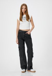 Hvid, kortærmet crop top med sort grafisk tekst, parret med løse sorte cargo-bukser med sidelommer og en løs pasform. Hvide sneakers.