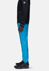 Blå utomhusbyxor med reflexdetaljer och dragkedjefickor, ihopparat med svarta sportskor. Överdelen är svart med en logotyp på ärmen.