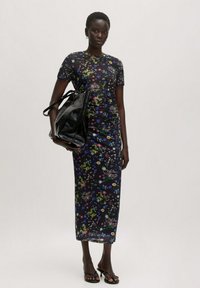 Een zwart, fitted jurk met een bloemenpatroon, met een top met korte mouwen en een lange rok. Vergezeld van een grote zwarte tote bag en sandalen met dunne hakken.