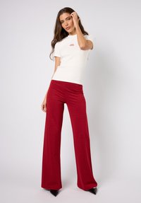 Hvit figursydd T-skjorte med korte ermer og røde vide bukser laget av et skinnende, teksturert stoff, kombinert med spisse svarte hæler.