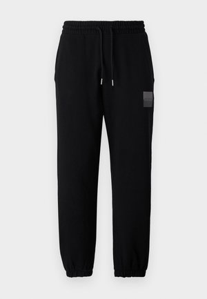 Zwarte joggers met een elastische tailleband en strikkoord, met taps toelopende pijpen en een klein logo-patch op de bovenbeen.
