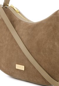 Brun ruskind skuldertaske med en gylden hardware lynlås og en justerbar beige rem. Har en metallisk logo-plade. Glat tekstur.