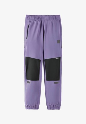 Fioletowe spodnie w kolorze bzu z czarnymi łatami na kolanach, elastycznym pasem i mankietami oraz detalami w postaci zamykanej na zamek bocznej kieszeni.