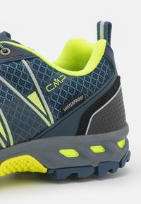 Męskie wodoodporne buty trekkingowe z ciemnoniebieską siateczkową cholewką, jasnóżółtymi akcentami, szarym środkowym podbiciem i czarną gumową podeszwą z teksturowanym gripem.