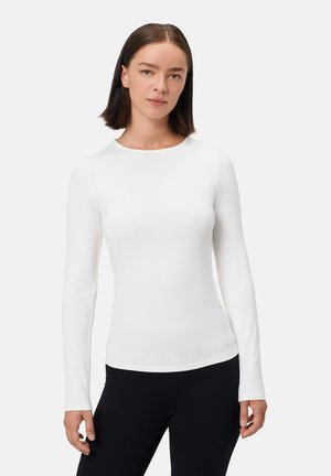Langärmliges, tailliertes Oberteil in Weiß, aus glattem Stoff gefertigt. Besitzt einen runden Halsausschnitt und eine dehnbare Textur, kombiniert mit schwarzen Leggings.