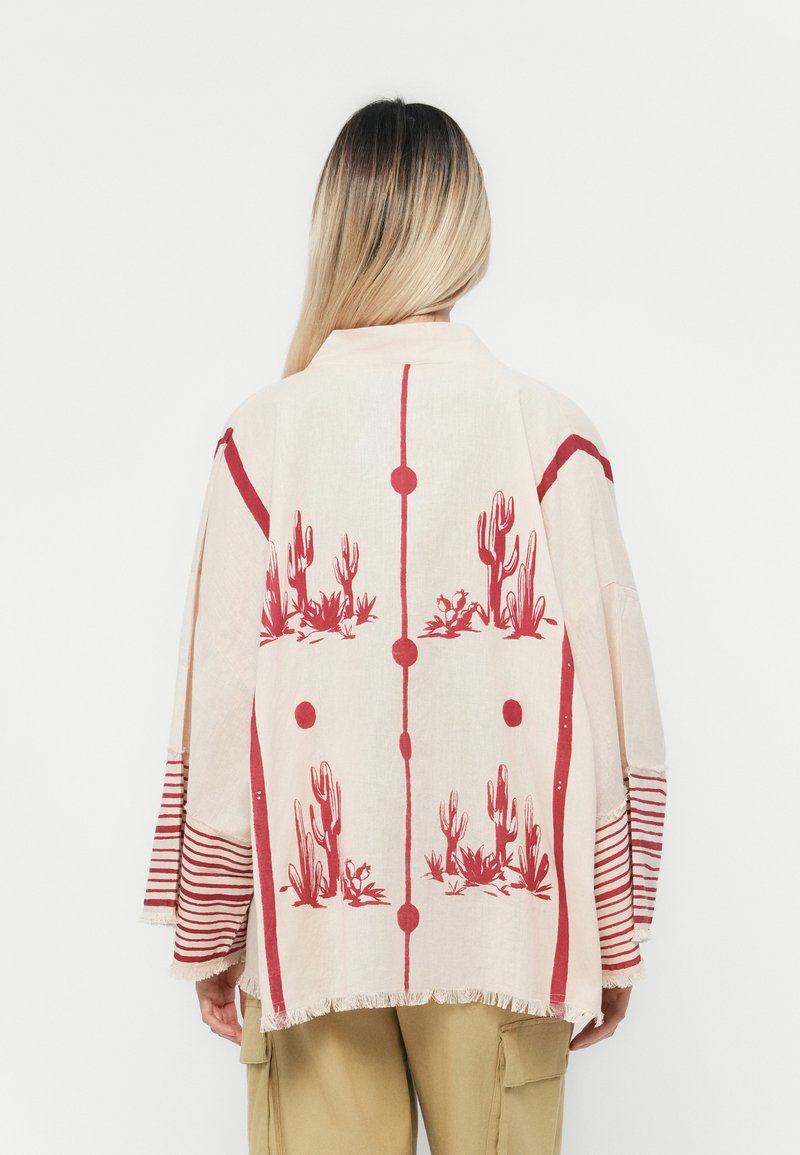 Svijetlosmeđi kimono s crvenim motivom kaktusa, s dugim rukavima sa prugastim detaljima i resicama na rubovima. Opušteni kroj.