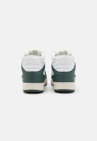 Para białych i ciemnozielonych sneakersów typu high-top pokazana z tyłu na jednolitym jasnym tle.