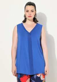 Top blu senza maniche con scollatura a V, una striscia verticale frontale e una texture liscia, abbinato a pantaloni floreali a fantasia.