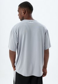 Camisa gris de manga corta con un corte holgado. Hecha de un material suave y ligero, presenta un diseño simple con costuras mínimas y un escote tipo barco.