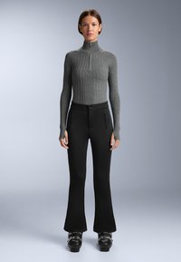 Grå ribbad polotröja med tight passform och stiligt hög krage, matchad med svarta utsvängda byxor med dragkedjeförsedda framfickor och kontrasterande sömmar.