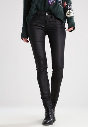 Jeans negros ajustados hechos de una tela lisa y elástica. Presenta una cintura de altura media, cinco bolsillos y un ajuste elegante. Combinados con un suéter verde texturizado.