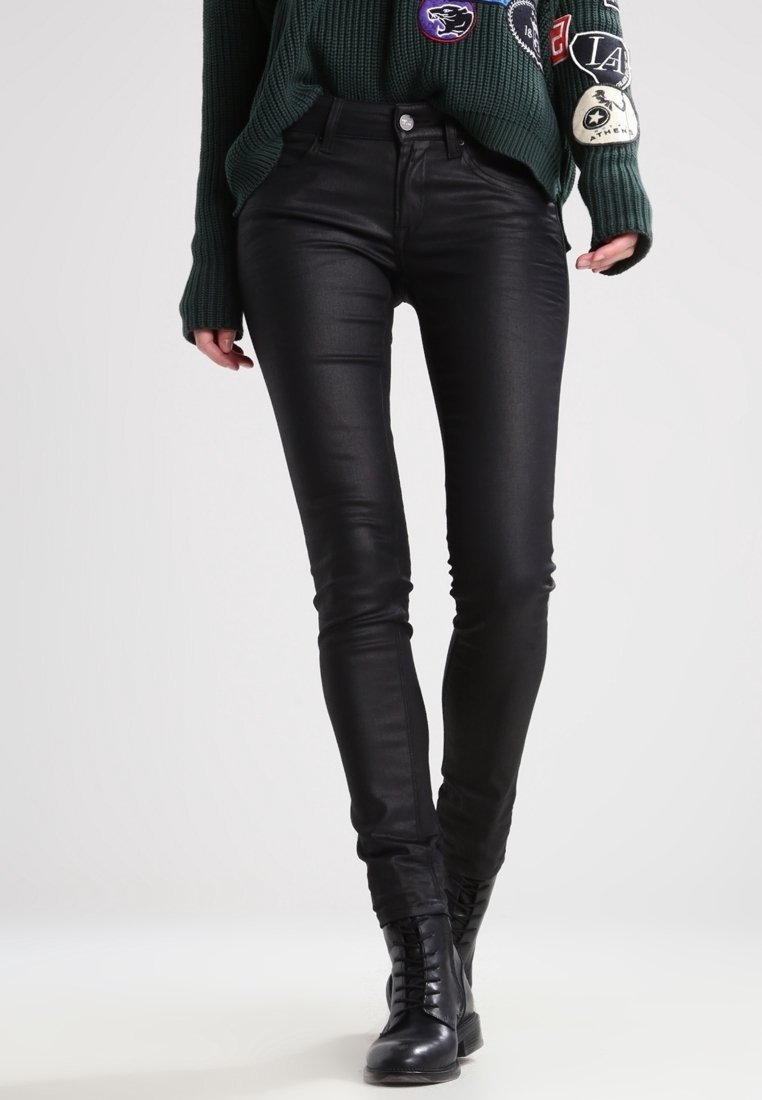 Jeans negros ajustados hechos de una tela lisa y elástica. Presenta una cintura de altura media, cinco bolsillos y un ajuste elegante. Combinados con un suéter verde texturizado.