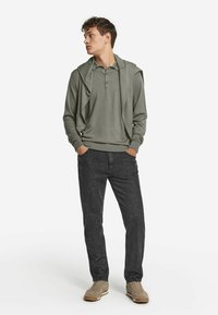 Ljusgrön långärmad polo med tre knappar, lagd över en tröja. Mörkgrå slim-fit jeans och beige sneakers fulländar looken.